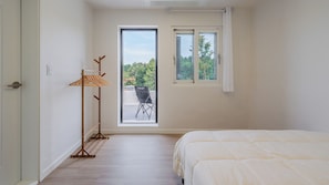Quarto com cama, varal de madeira, janela e varanda com cadeira.
