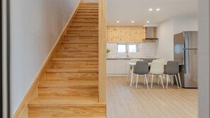 A modern kitchen with a wooden staircase, a dining area with chairs, and a stainless steel refrigerator. - Gangneung Sacheon Bom House Pension (Gangneung)