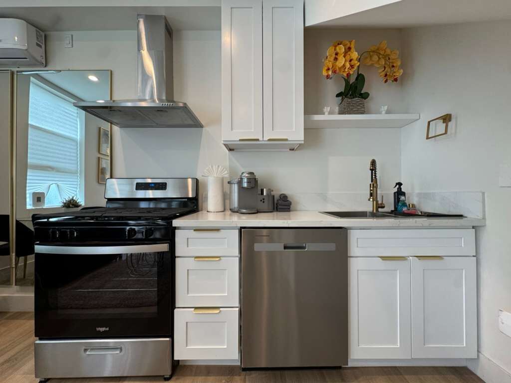 Une cuisine moderne avec des meubles blancs, un lave-vaisselle en acier inoxydable et une cuisinière noire.