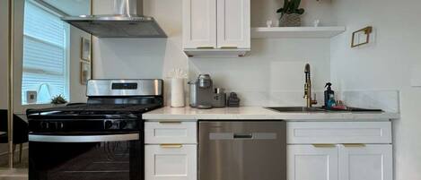 Une cuisine moderne avec des meubles blancs, un lave-vaisselle en acier inoxydable et une cuisinière noire.