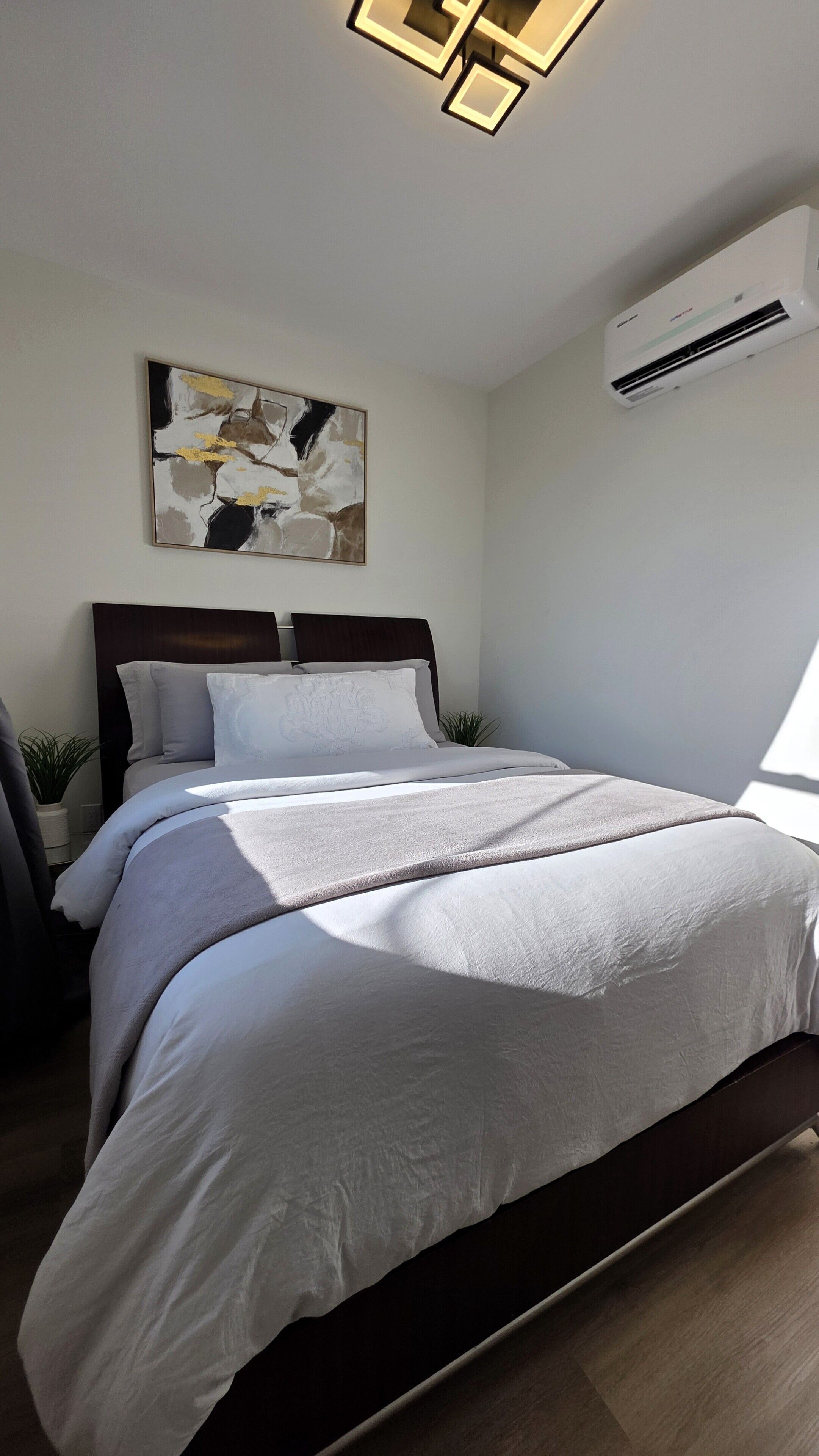Quarto com cama, ar condicionado fixado na parede e luminária no teto.