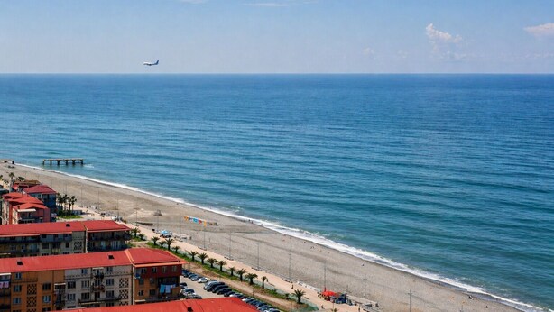 Ein Hotel an der Küste mit Blick auf den Strand, einem Steg und einem entfernt fliegenden Flugzeug.