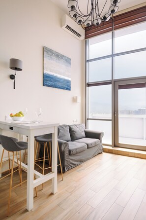 Ein moderner Wohnraum mit Essbereich, einem grauen Sofa, einem großen Fenster und einem Gemälde an der Wand.