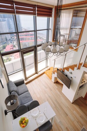 Een modern appartement met een eethoek, een bank en een groot raam met uitzicht op de stad.