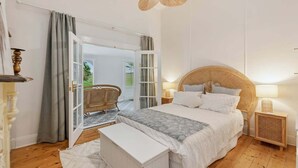A bedroom with a bed, bedside tables, a ceiling fan, and a view through an open door. - Cork Hill Retreat - Charming & Historic with Natural Beauty (Cape Bridgewater)