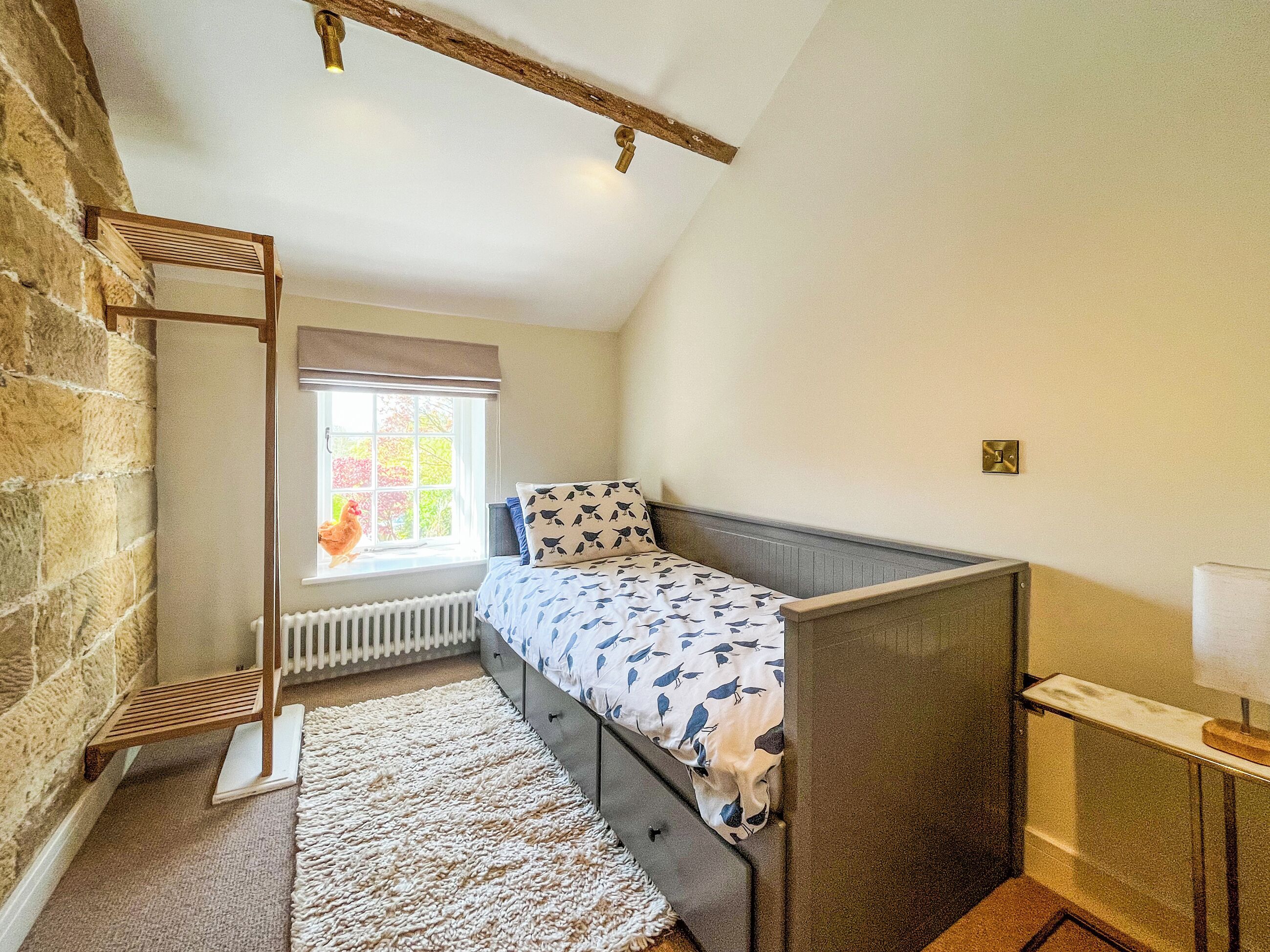 A bedroom with a bunk bed, a radiator, a window with a view of trees, and a wooden ladder.