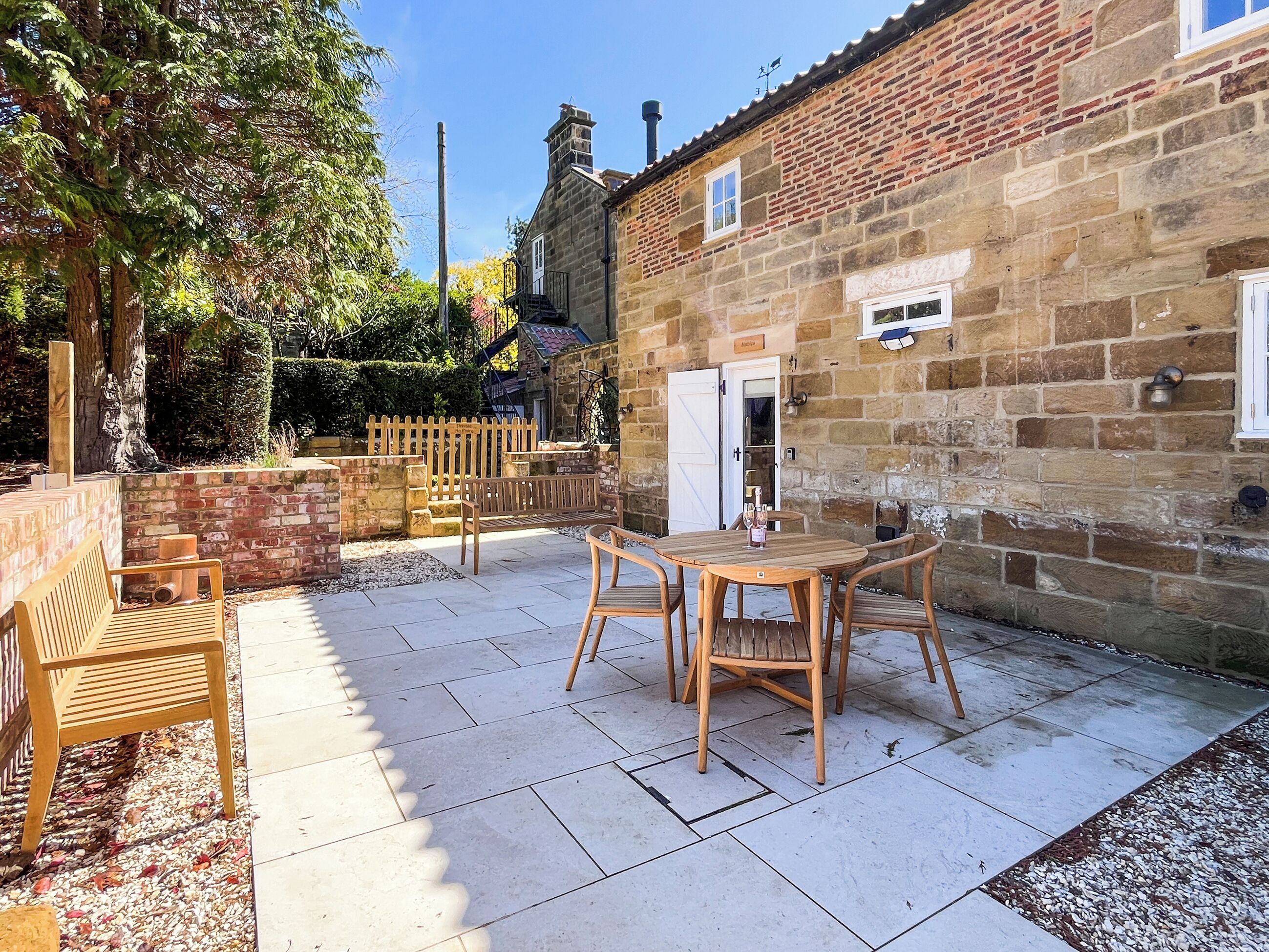 A stone building with a patio area featuring wooden furniture and a white door.