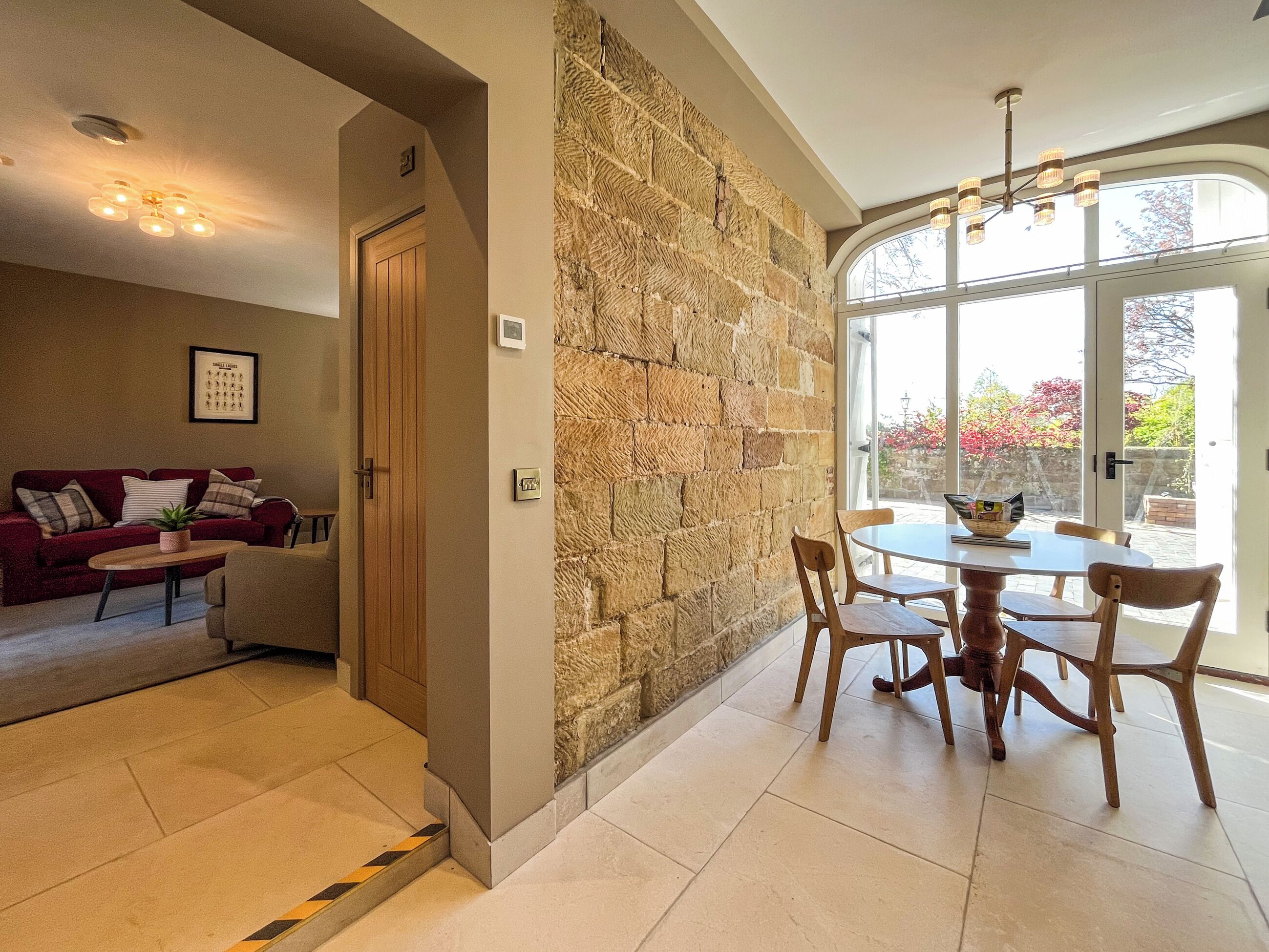 A living room with a stone wall, a dining area with a table and chairs, a red sofa, and a ceiling light fixture.