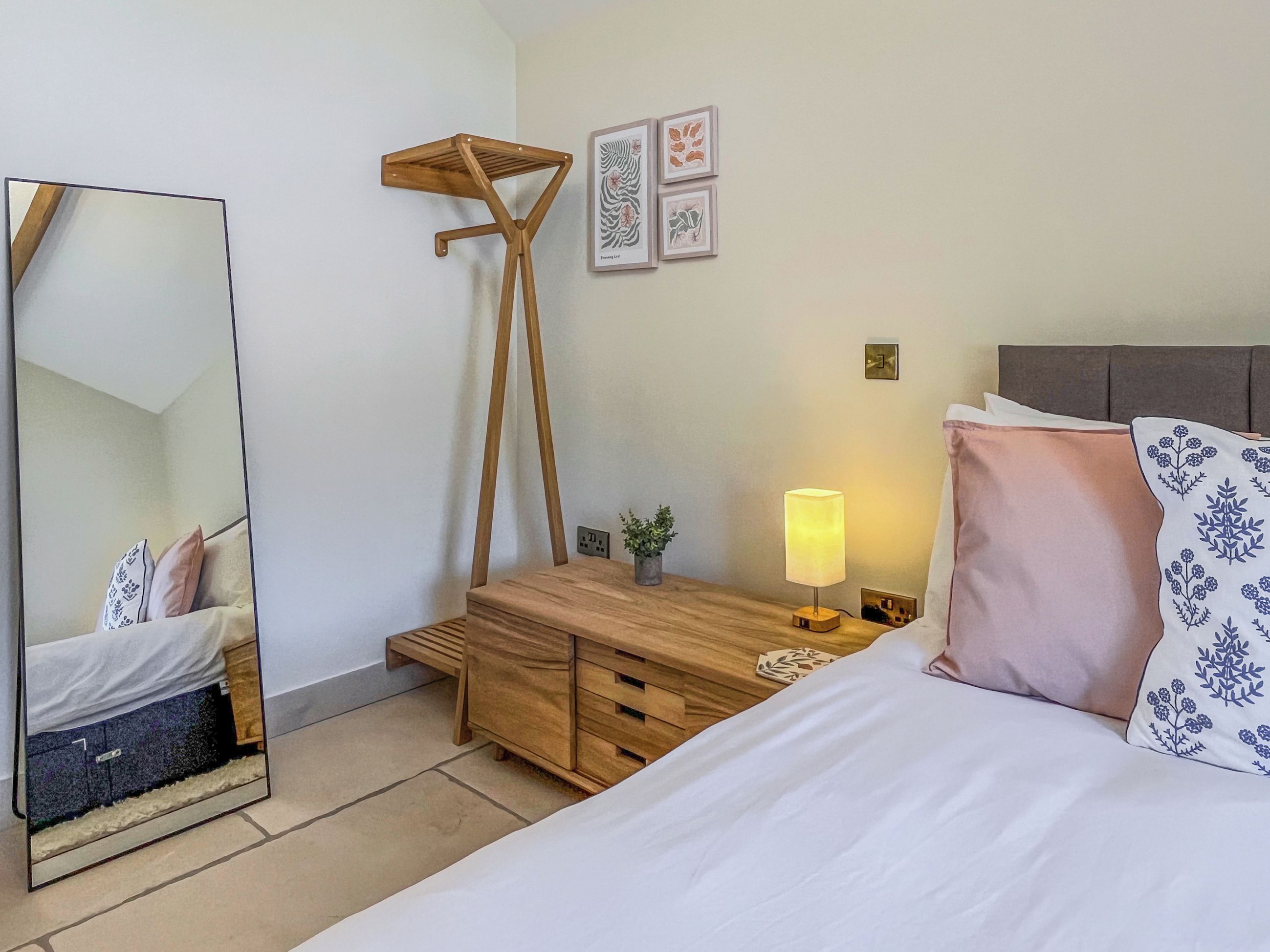 Een slaapkamer met een bed, nachtkastje, lamp, kaptafel, spiegel en wanddecoratie.