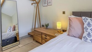 A bedroom with a bed, bedside table, lamp, dresser, mirror, and wall art.