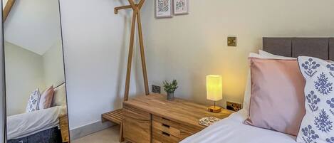 Een slaapkamer met een bed, nachtkastje, lamp, kaptafel, spiegel en wanddecoratie.