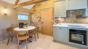 A kitchen with a stone wall, wooden ceiling beams, a wooden door, and a white countertop.