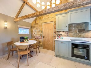 A kitchen with a stone wall, wooden ceiling beams, a wooden door, and a white countertop.