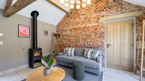 A cozy living room with a brick wall, a sofa, a table with a plant, a fireplace, and a wooden door.