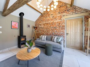 A cozy living room with a brick wall, a sofa, a table with a plant, a fireplace, and a wooden door.