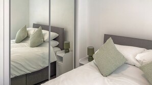 Ein Schlafzimmer mit Bett, Kissen, Nachttisch, Lampe und einer Schiebetür.