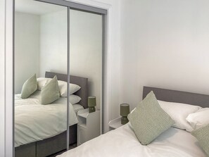 Ein Schlafzimmer mit Bett, Kissen, Nachttisch, Lampe und einer Schiebetür.
