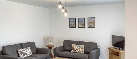 A modern living room with two grey sofas, a wooden coffee table, a side table with a lamp, and a TV stand.