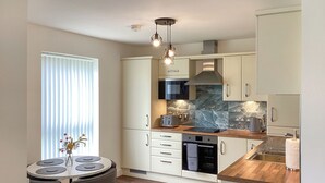 Eine moderne Küche mit weißen Schränken, einer Holzarbeitsplatte, einem eingebauten Backofen und einem Essbereich mit rundem Tisch und Stühlen.
