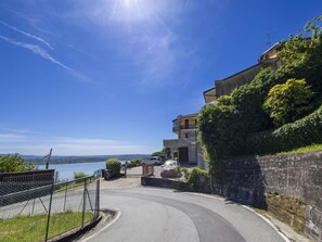 Uma estrada sinuosa conduz a um edifício com vista para um corpo d'água e colinas distantes.