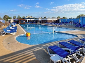 A swimming pool with blue lounge chairs, a water fountain, and a building with a blue roof in the background. - 2 bedroom accommodation in Paignton (Paignton)