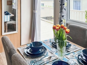 A dining area with a table set for two, a vase with tulips, and a view of a balcony. - 2 bedroom accommodation in Paignton (Paignton)