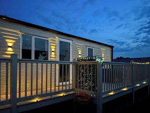 A mobile home with a deck, illuminated by exterior lights, and a railing. - 2 bedroom accommodation in Paignton (Paignton)