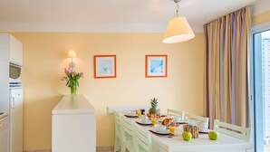 Un comedor con una mesa blanca, sillas, una lámpara y vistas al exterior a través de una ventana con cortinas.