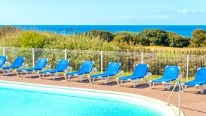Una piscina con sillas azules y vista al océano.