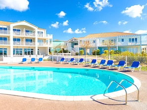 A swimming pool with lounge chairs, a multi-story building with balconies, and a clear blue sky. - Coastal Getaway in the Vendee (Les Sables-d'Olonne)