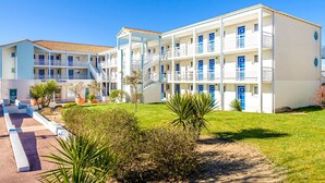 Un hotel de varios pisos con balcones, una escalera central y un césped bien cuidado.