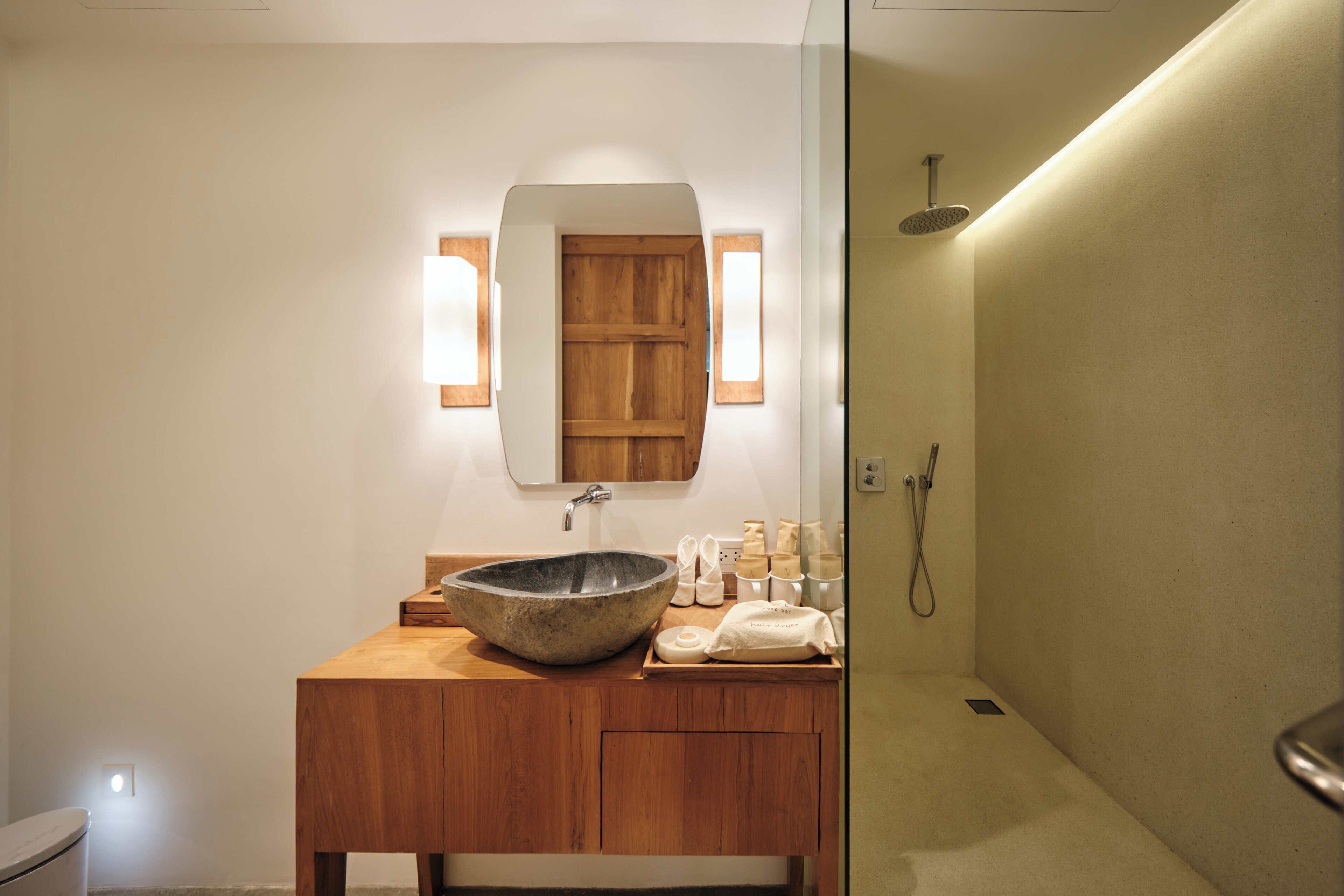 A bathroom with a wooden vanity, a large mirror, a stone basin, and a shower area.