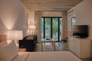 A hotel room with a bed, a desk, a TV, a sofa, and a view of greenery outside.