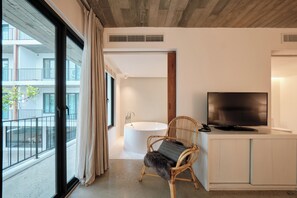 A modern bathroom with a bathtub, a television, and a wicker chair.