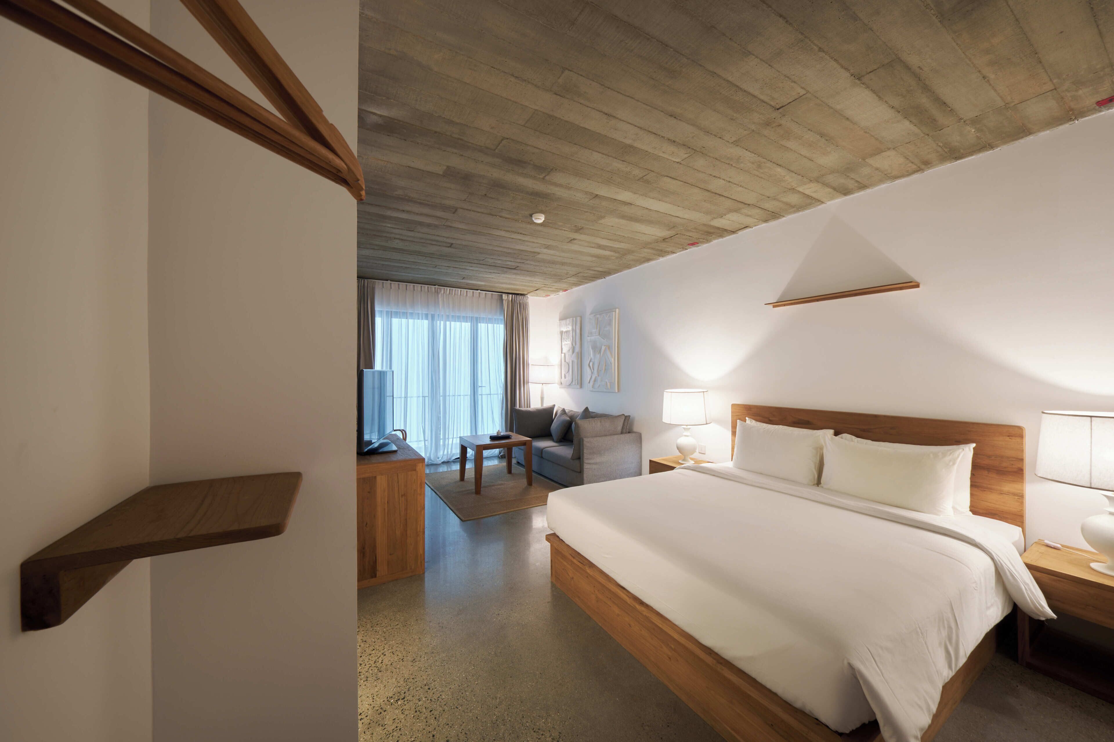 Une chambre d’hôtel avec un plafond en bois, un grand lit, un bureau, une chaise et une fenêtre avec des rideaux.