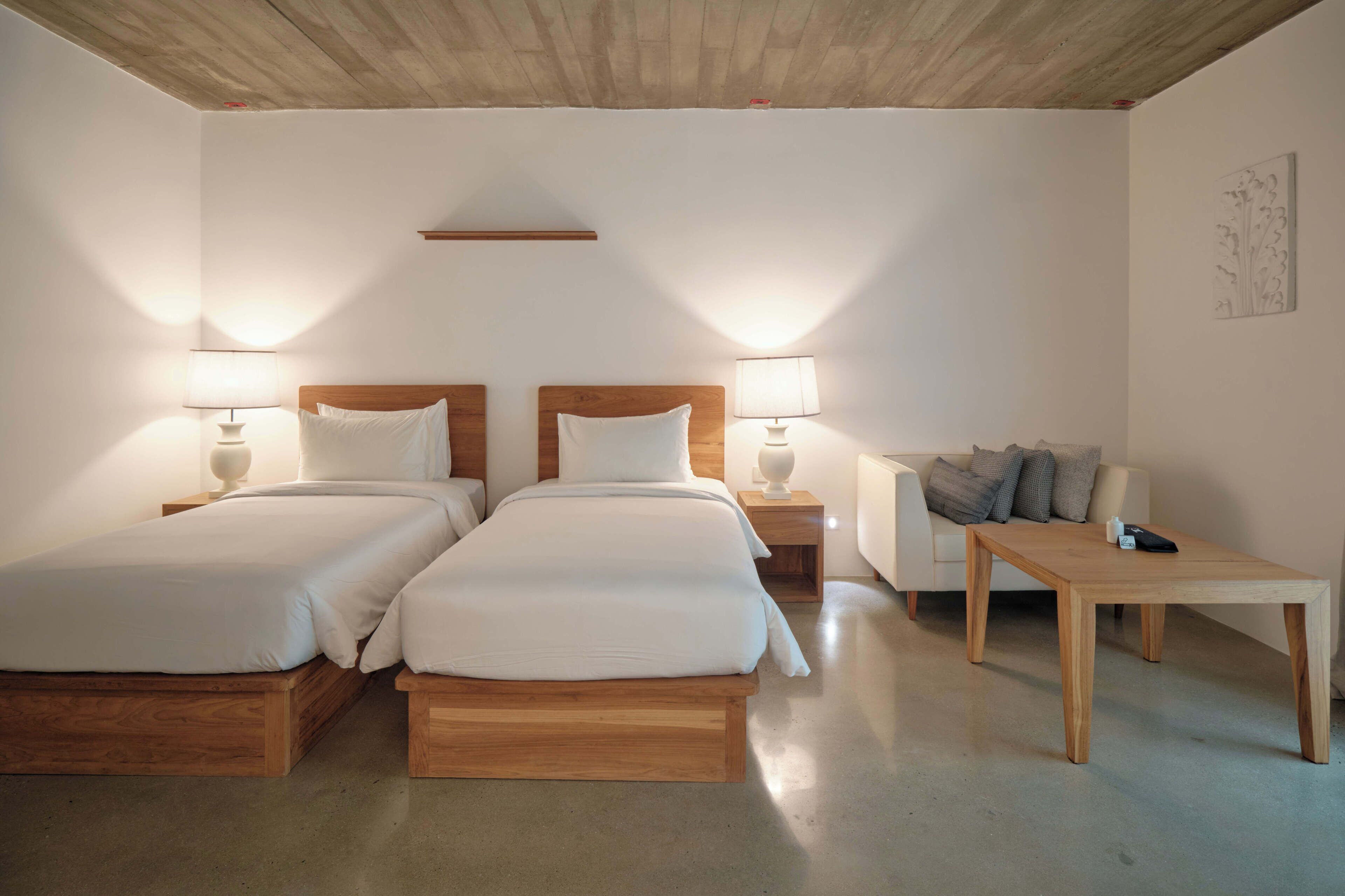 A room with two wooden beds, a small table, and a sofa.