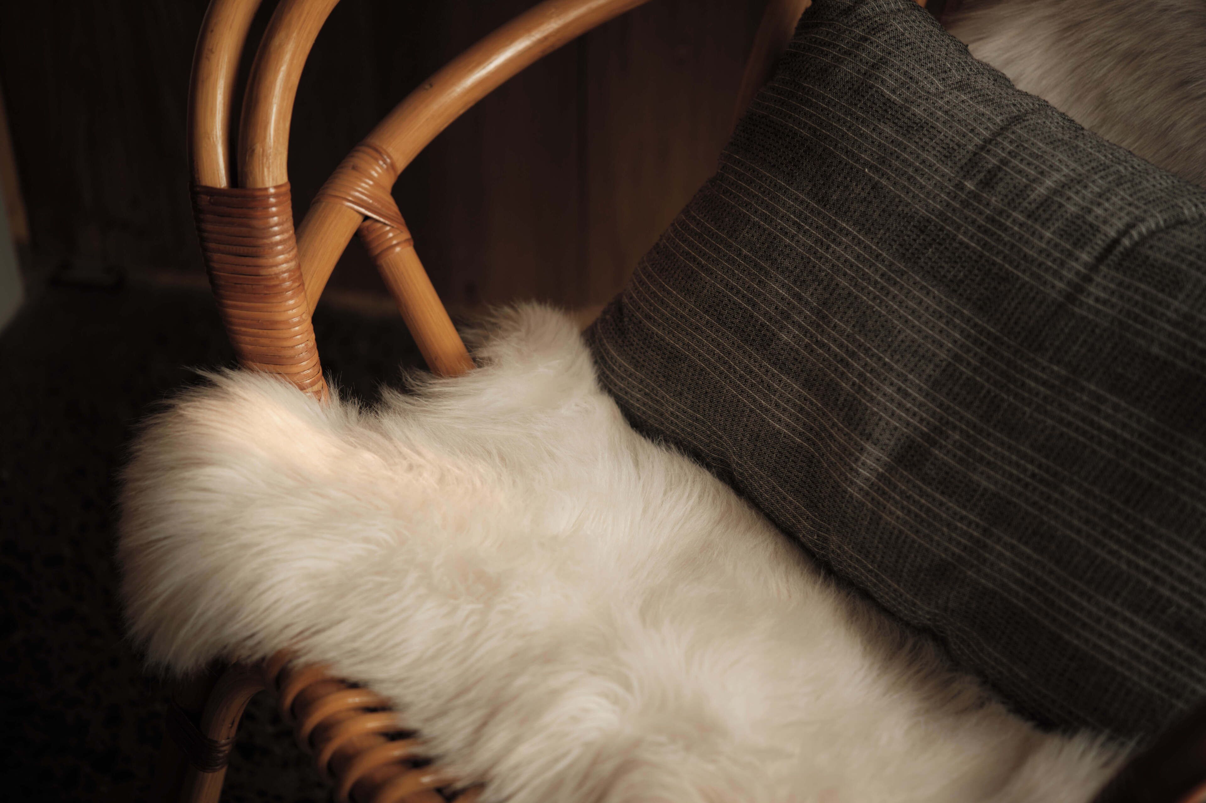 A wicker chair with a white furry seat and a grey cushion.