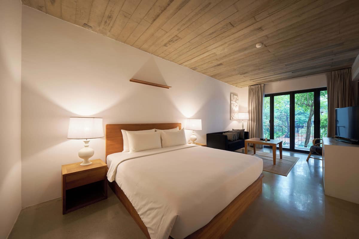 Ein Hotelzimmer mit Holzbalkendecke, einem großen Bett mit weißen Laken, einem Schreibtisch mit Stuhl und einem Fernseher.