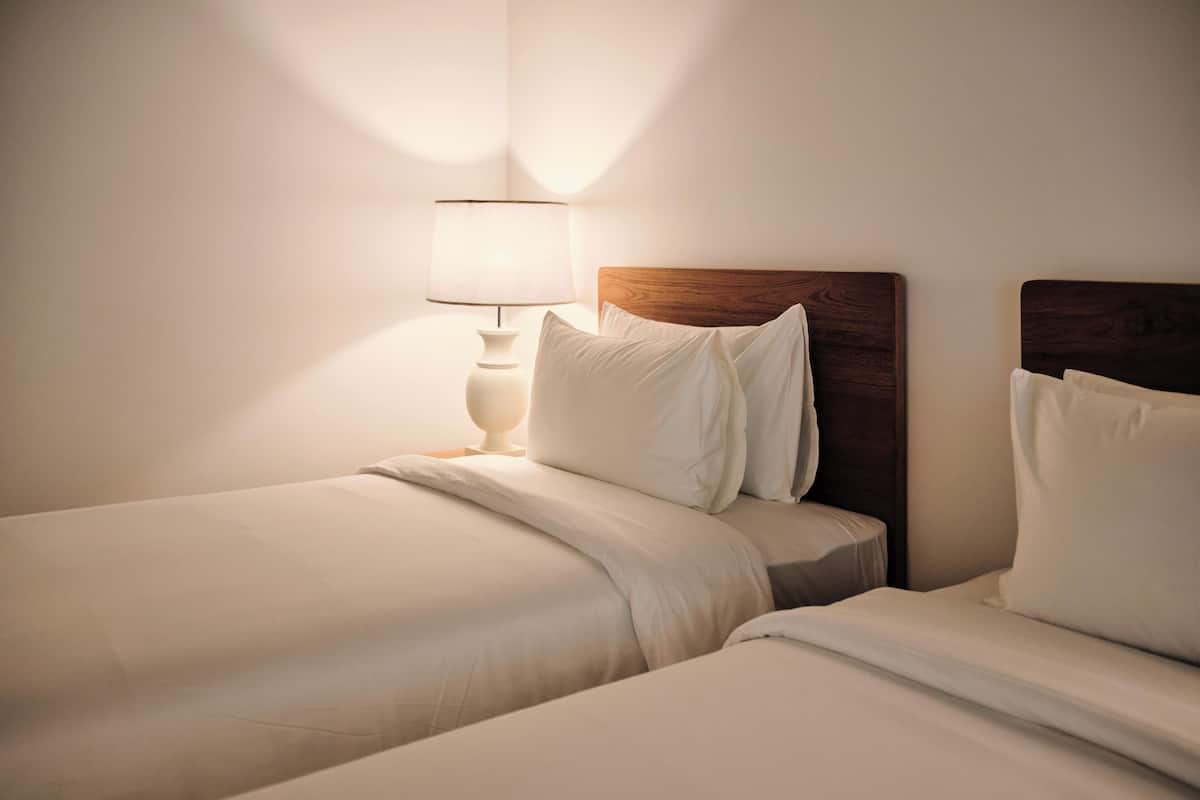 Ein Hotelzimmer mit zwei Einzelbetten, einem Nachttisch mit Lampe und einem Holzkopfteil.