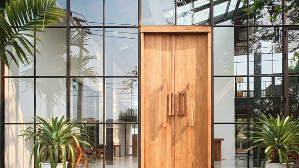 Un edificio moderno con grandes ventanales, una puerta de madera y plantas en macetas.