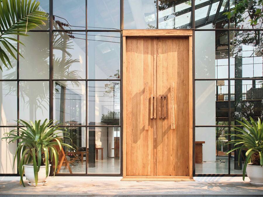 Um edifício moderno com grandes janelas de vidro, uma porta de madeira e plantas em vasos.