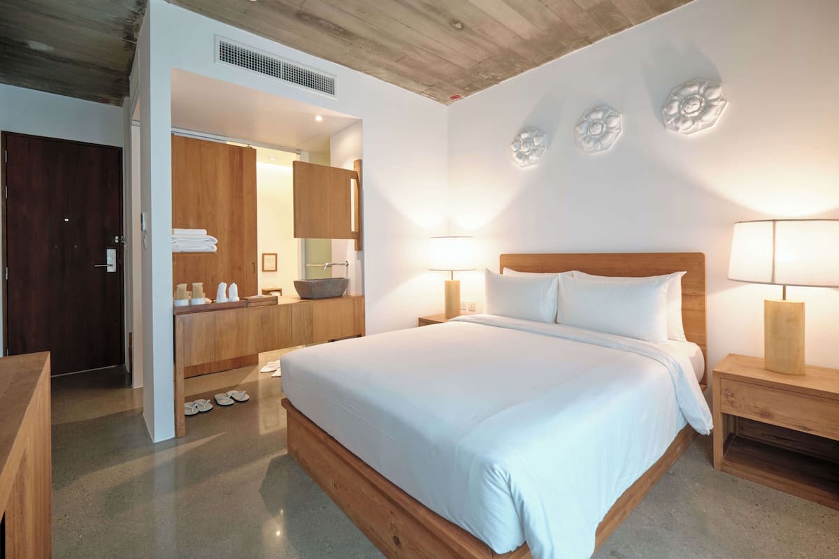 Ein Schlafzimmer mit einem hölzernen Bett, Nachttischlampen, einem Nachttisch aus Holz, einem Holzschrank und einem Badezimmer mit einer Holztür.