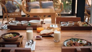 Una escena de desayuno con una mesa de madera, sillas de mimbre y vistas a la vegetación.