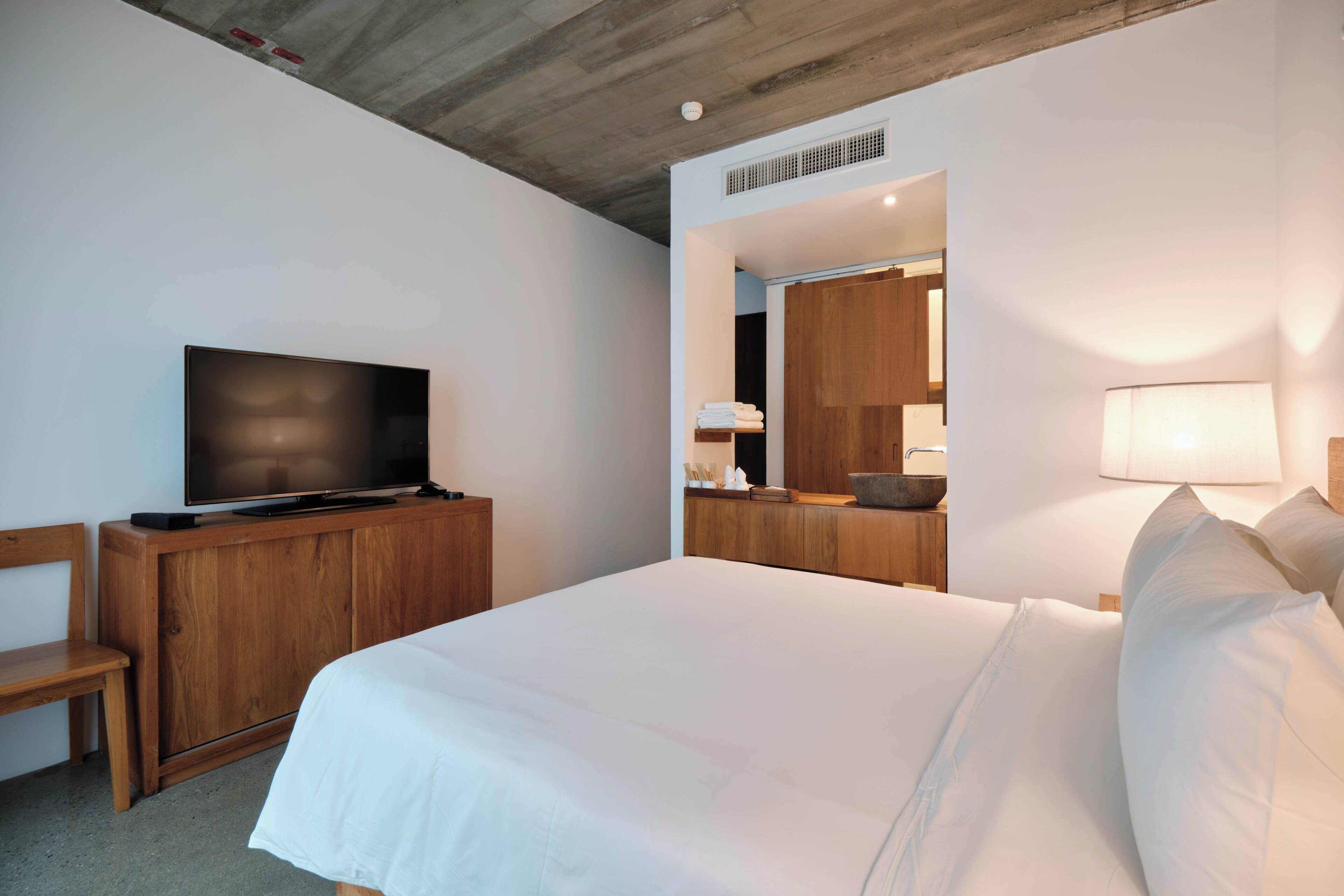 A hotel room with a large bed, a television on a wooden cabinet, a mirror, and a bedside lamp.