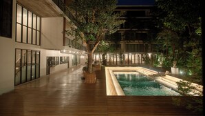 Un edificio moderno con una terraza de madera, una piscina y abundante vegetación.