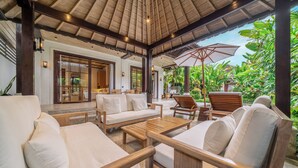 Een overdekt terras met houten meubels en parasols, omringd door weelderige begroeiing.