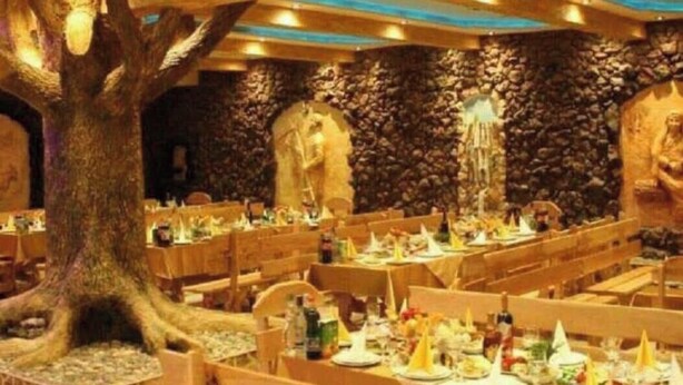 A restaurant with wooden tables and chairs, a large tree centerpiece, stone walls, and a statue. - ZANGEZUR HOTEL GORIS (Goris)