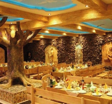 A restaurant with wooden tables and chairs, stone walls, and a large tree centerpiece.. ZANGEZUR HOTEL GORIS