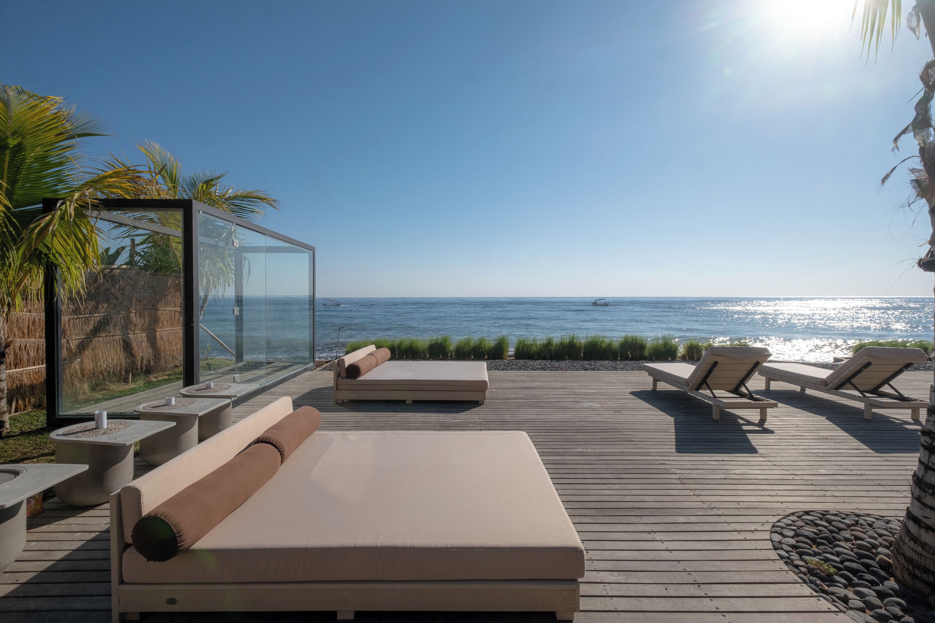 A wooden deck with lounge chairs and a glass balustrade overlooking the sea.