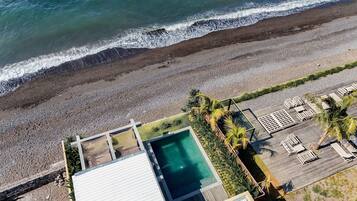 Luchtbeeld van een pand aan het strand met een zwembad, ligbedden en een houten terras.